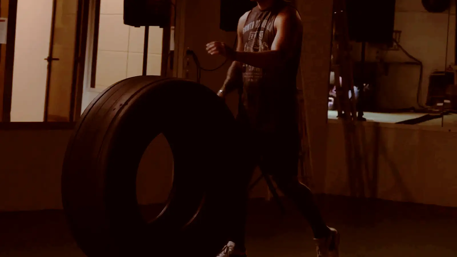 A member rolling a training tyre across the gym floor in low light.